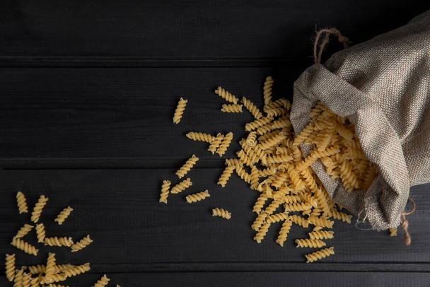 Een zak vol rauwe droge pasta fusilli geplaatst op een houten donkere tafel. Hoge kwaliteit foto - Foto, afbeelding