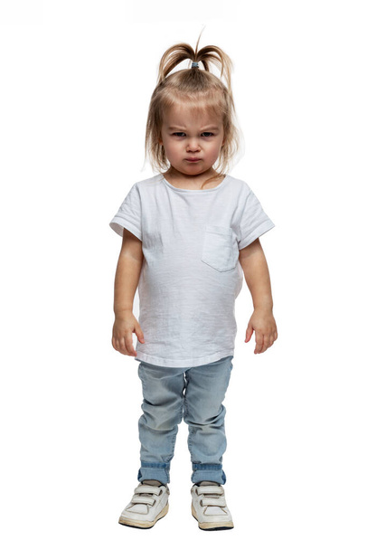 Angry little girl. A 4-year-old child stands in jeans and a white T-shirt. Aggression, stress and resentment. Isolated on white background. Vertical. - Valokuva, kuva