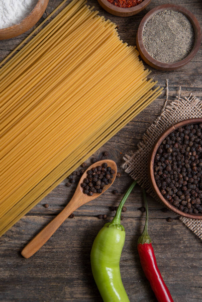 Raw spaghetti and bowl of peppercorns placed on wooden surface. High quality photo - 写真・画像