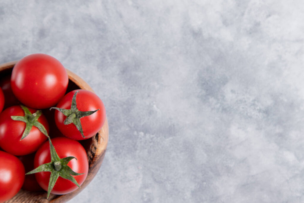 Puinen kulho täynnä tuoreita mehukkaita punaisia tomaatteja sijoitettu kivi pöydälle. Laadukas kuva - Valokuva, kuva