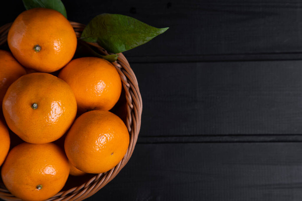 A wicker basket full of fresh tangerine fruits with leaves placed on a dark wooden table . High quality photo - Φωτογραφία, εικόνα