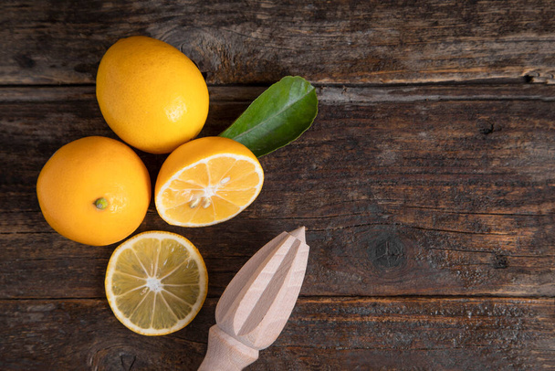 Fresh lemon fruits with leaves and wooden reamer placed on a wooden table . High quality photo - Valokuva, kuva