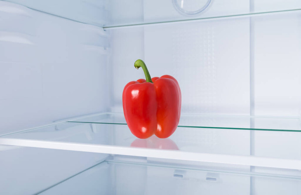 against the background of a white refrigerator, there is a red Bulgarian sweet pepper on a glass shelf, close-up - Foto, Imagem