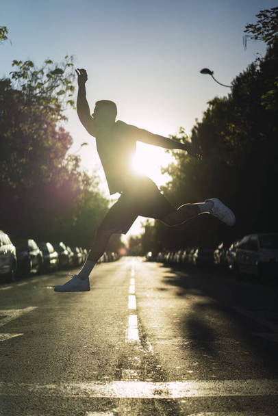 A vertical shot of a young sporty guy jumping in the middle of an asphalt road at sunset - Foto, Bild