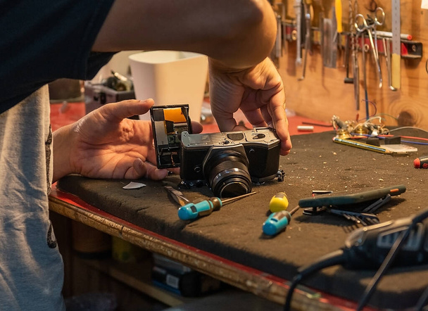 A close-up shot of a Hispanic male technician's hands repairing a camera at the service center. - 写真・画像
