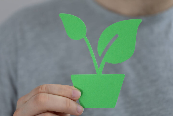 A male's hand holding a green paper plant - Φωτογραφία, εικόνα