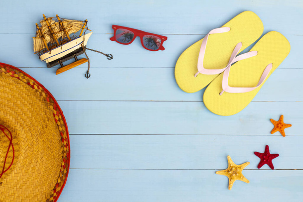 A cool view on painted light blue wood table with sunglasses, flip flops, sailboat, hat, and starfish - Photo, image