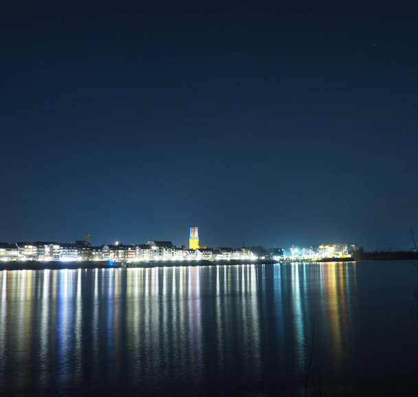 An evening view of a coastal town with bright lights reflecting on the surface under a clear sky - Fotografie, Obrázek