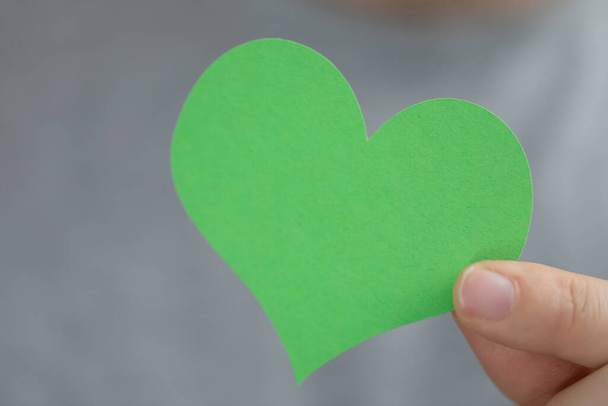 Un primer plano de una mano sosteniendo un corazón de papel verde. Energía verde, energía del futuro, mundo ecológico. - Foto, Imagen