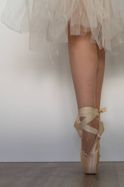 legs of girl dancing ballet with tulle skirt and pink shoes different dance steps wooden floor and white background with copy space - Φωτογραφία, εικόνα