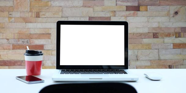 Front view φορητό υπολογιστή, φλιτζάνι καφέ και έξυπνο τηλέφωνο σε λευκό τραπέζι με τοίχο από τούβλα. - Φωτογραφία, εικόνα