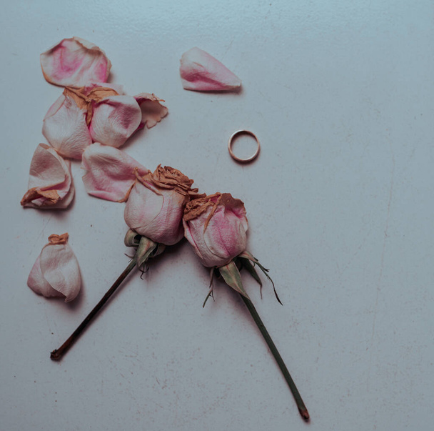 A closeup shot of rose petals and a ring on a white surface - Fotó, kép