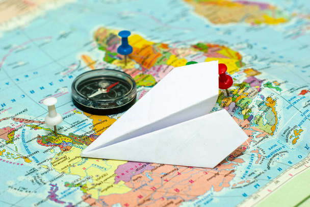Seyahat konsepti pusula ve kağıt uçak dünya haritasında, düğmeler seyahat yerlerini gösteriyor - Fotoğraf, Görsel