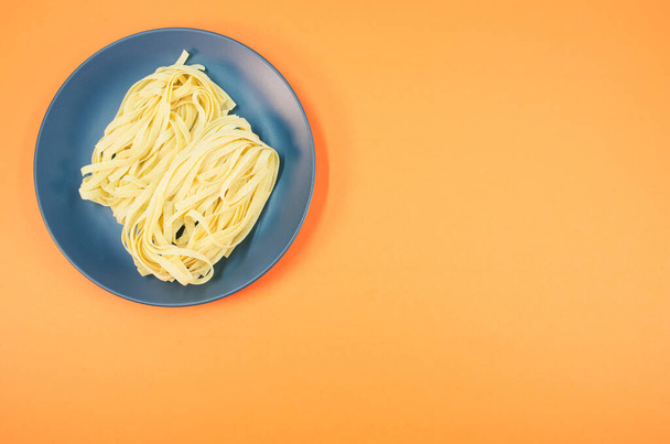 A plate of raw pasta isolated on an orange background with free space for text - Fotó, kép