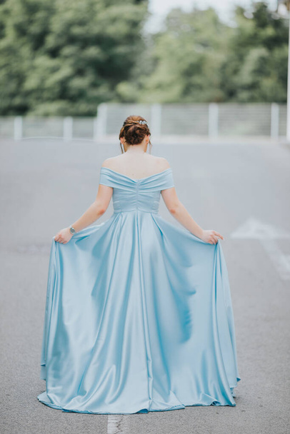 A vertical shot of a Caucasian young female dressed in a beautiful sky-blue floor-length evening gown - Foto, Imagen