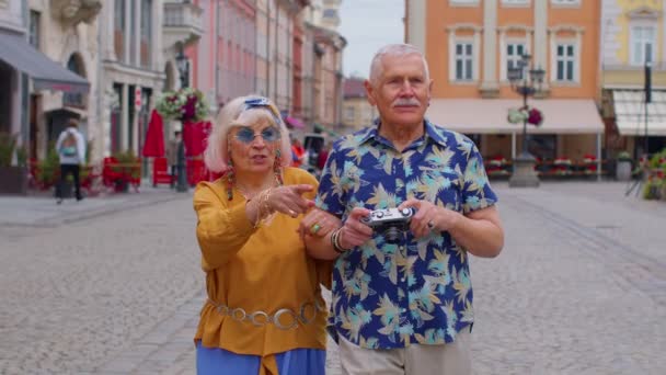 Ältere stilvolle Touristen, Mann und Frau, die mit einer alten Filmkamera Fotos machen und die Straße entlang spazieren - Filmmaterial, Video