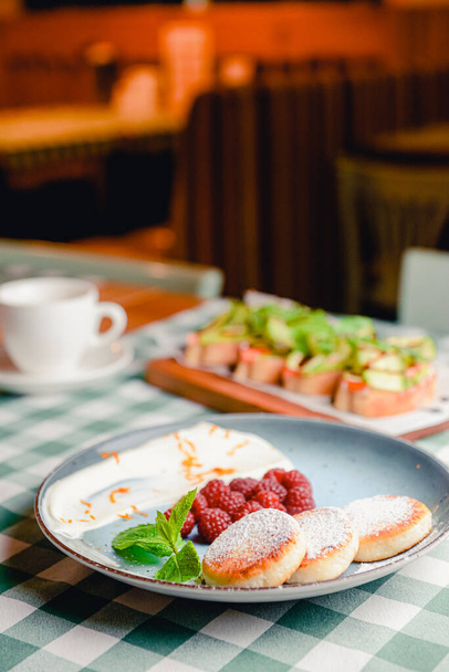 Traditional sweet syrniki or cottage cheese pancakes served with sweet cream and fresh raspberries in a white plate over table with green plaid tablecloth. - Φωτογραφία, εικόνα