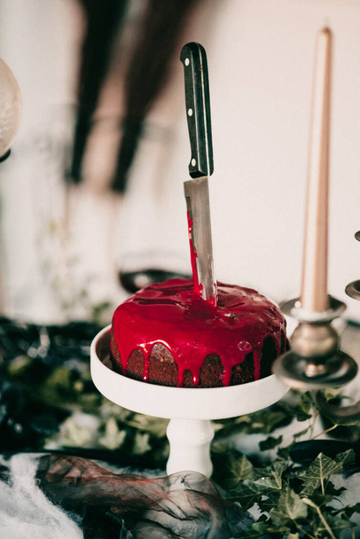 A vertical shot of spooky Halloween decorations, a chocolate cake with red frosting, and a knife - Photo, Image