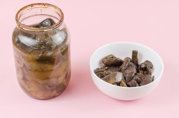Botulism, food poisoning from canned foods concept. Glass jar and white bowl of homemade pickled mushrooms.  Spoiled blackened forest mushrooms - Photo, Image