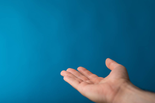 A male showing an outstretched hand with an open palm on a blue background - Foto, immagini