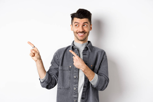 Happy handsome man smiling and pointing left at banner, showing cool product, standing on white background - Фото, зображення
