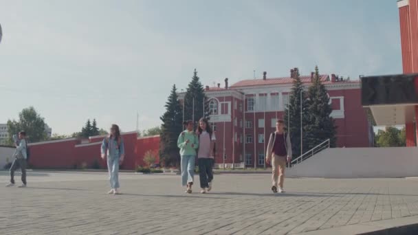 Laaghoekige opname van groep middelbare scholieren die weglopen van het schoolgebouw - Video