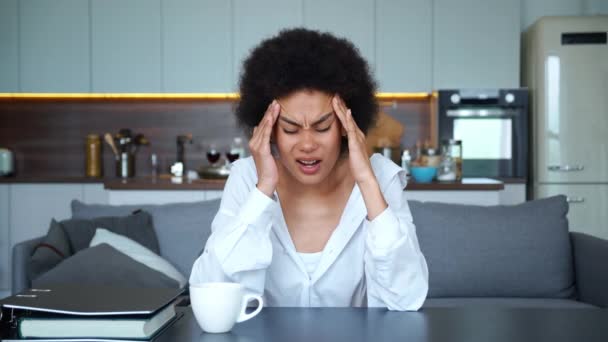 Afroameričanka, která seděla u stolu na pozadí kuchyně a dívala se do kamery, pocítila náhlou bolest hlavy, migrénu, držela se za ruce u hlavy a masírovala si spánky.. - Záběry, video