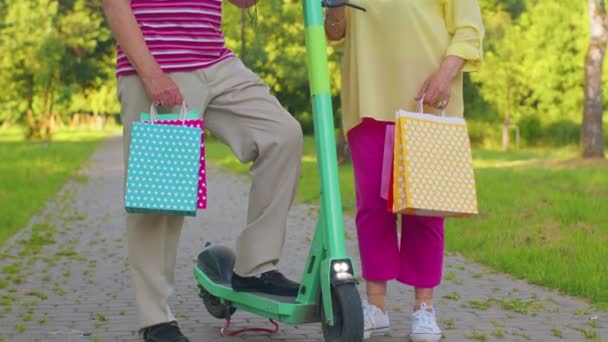 Senior abuela pareja con estilo, abuelo después de comprar con bolsas usando scooter para montar a caballo - Metraje, vídeo