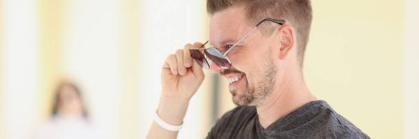 Young man with stylish hairstyle putting on sunglasses - Фото, изображение
