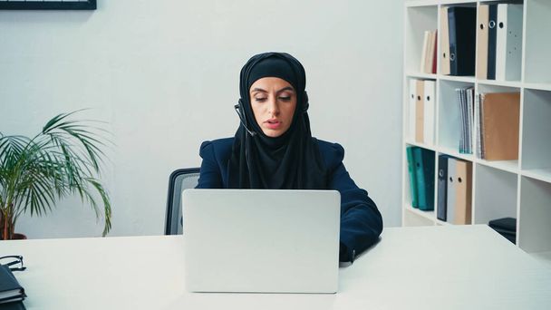 Çağrı merkezinde laptop kullanan, kulaklık takan Müslüman bir iş kadını.  - Fotoğraf, Görsel
