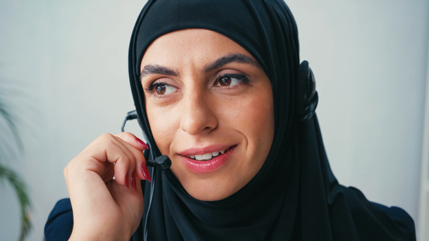 Muslim operator of call center using headset and smiling in office  - 写真・画像