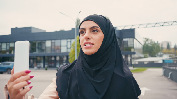 Молодая мусульманка в хиджабе разговаривает во время видеозвонка на городской улице  - Фото, изображение