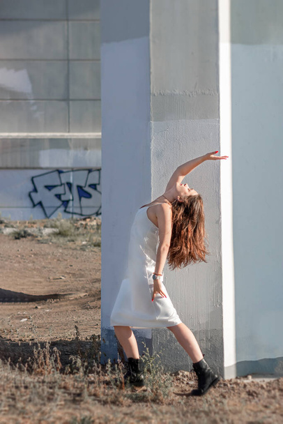 Woman in white dress and with long hair posing under the bridge against the background of concrete pillars - Fotó, kép