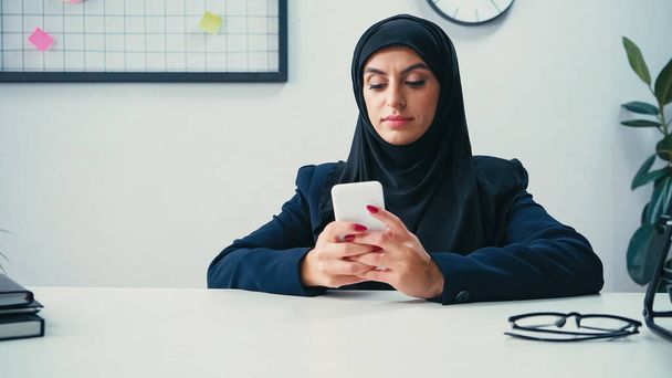 Muzułmańska bizneswoman za pomocą smartfona w pobliżu notebooków na stole  - Zdjęcie, obraz