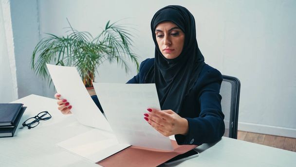 Μουσουλμάνα γυναίκα με μαντίλα που εργάζεται με έγγραφα στο γραφείο  - Φωτογραφία, εικόνα