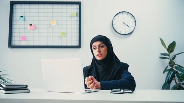впевнена мусульманська бізнес-леді, що має відеодзвінок на ноутбук в офісі
  - Фото, зображення
