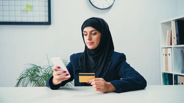 Çevrimiçi alışveriş yaparken akıllı telefon ve kredi kartı kullanan Müslüman kadın  - Fotoğraf, Görsel