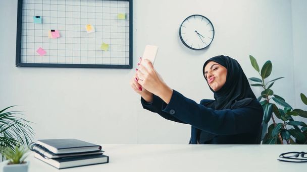 donna d'affari musulmana che fa il broncio alle labbra e si fa selfie sullo smartphone in ufficio  - Foto, immagini