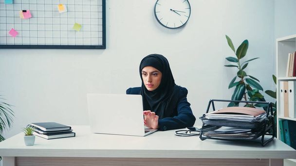 мусульманська бізнес-леді в хіджабі, використовуючи ноутбук в сучасному офісі
  - Фото, зображення