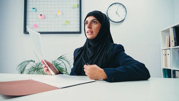 mulher de negócios muçulmana no hijab segurando documento e caneta no escritório moderno  - Foto, Imagem