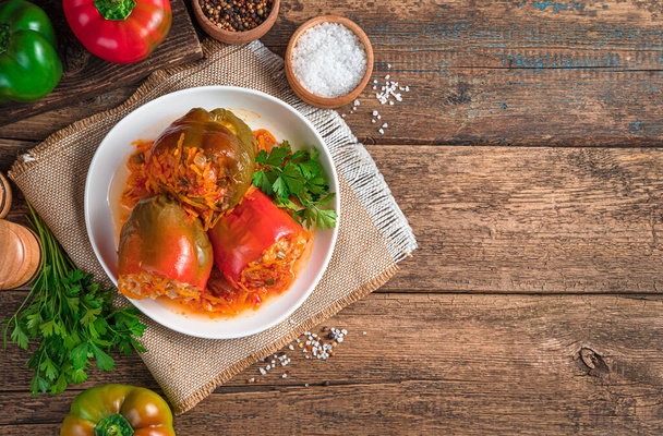Drei Paprika gefüllt mit Fleisch, Reis und Gemüse in einem weißen Teller auf einem hölzernen Hintergrund. - Foto, Bild