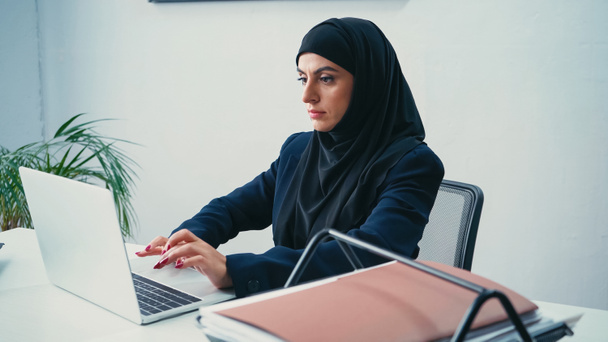 молодая мусульманская бизнесвумен в хиджабе печатает на ноутбуке в современном офисе  - Фото, изображение