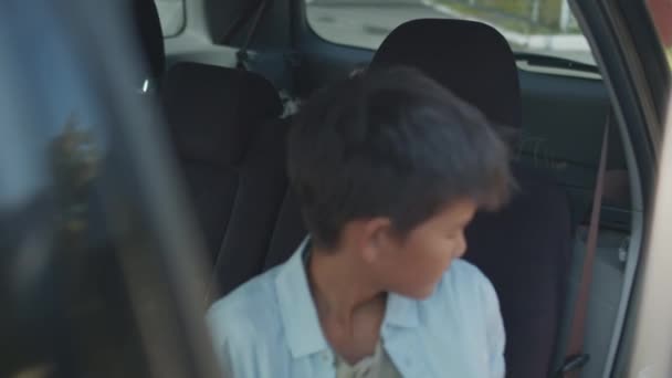Портативный снимок 12-летнего азиатского мальчика с рюкзаком, садящегося на пассажирское сиденье автомобиля и пристегивающего ремень безопасности после того, как его забрал из школы его родитель или опекун - Кадры, видео