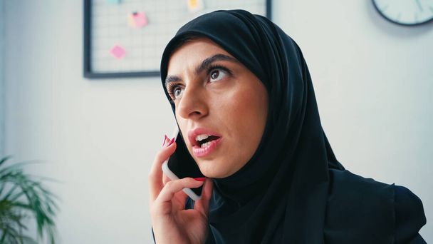 Мусульманская предпринимательница в хиджабе разговаривает по мобильному телефону в офисе - Фото, изображение