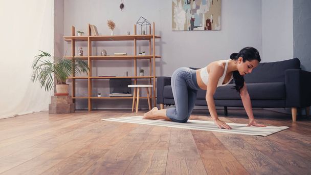 Young woman standing on fitness mat in living room  - Photo, Image