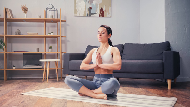 Çıplak ayaklı kadın evde yoga minderi üzerinde meditasyon yapıyor.  - Fotoğraf, Görsel