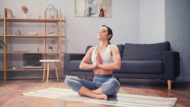Босоногая спортсменка практикующая йогу в гостиной  - Фото, изображение