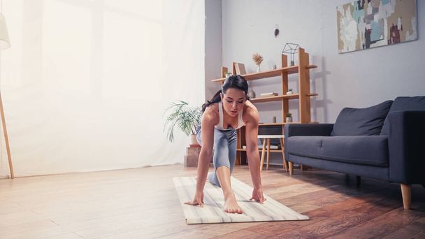 Sportswoman esercitare vicino divano sul tappeto fitness a casa  - Foto, immagini