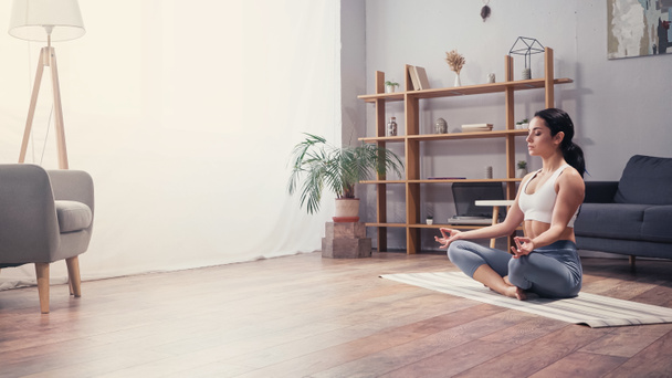 Seitenansicht einer meditierenden jungen Frau im Wohnzimmer  - Foto, Bild