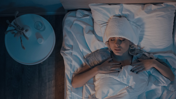 Κάτοψη της άρρωστης γυναίκας ξαπλωμένης στο κρεβάτι τη νύχτα  - Φωτογραφία, εικόνα